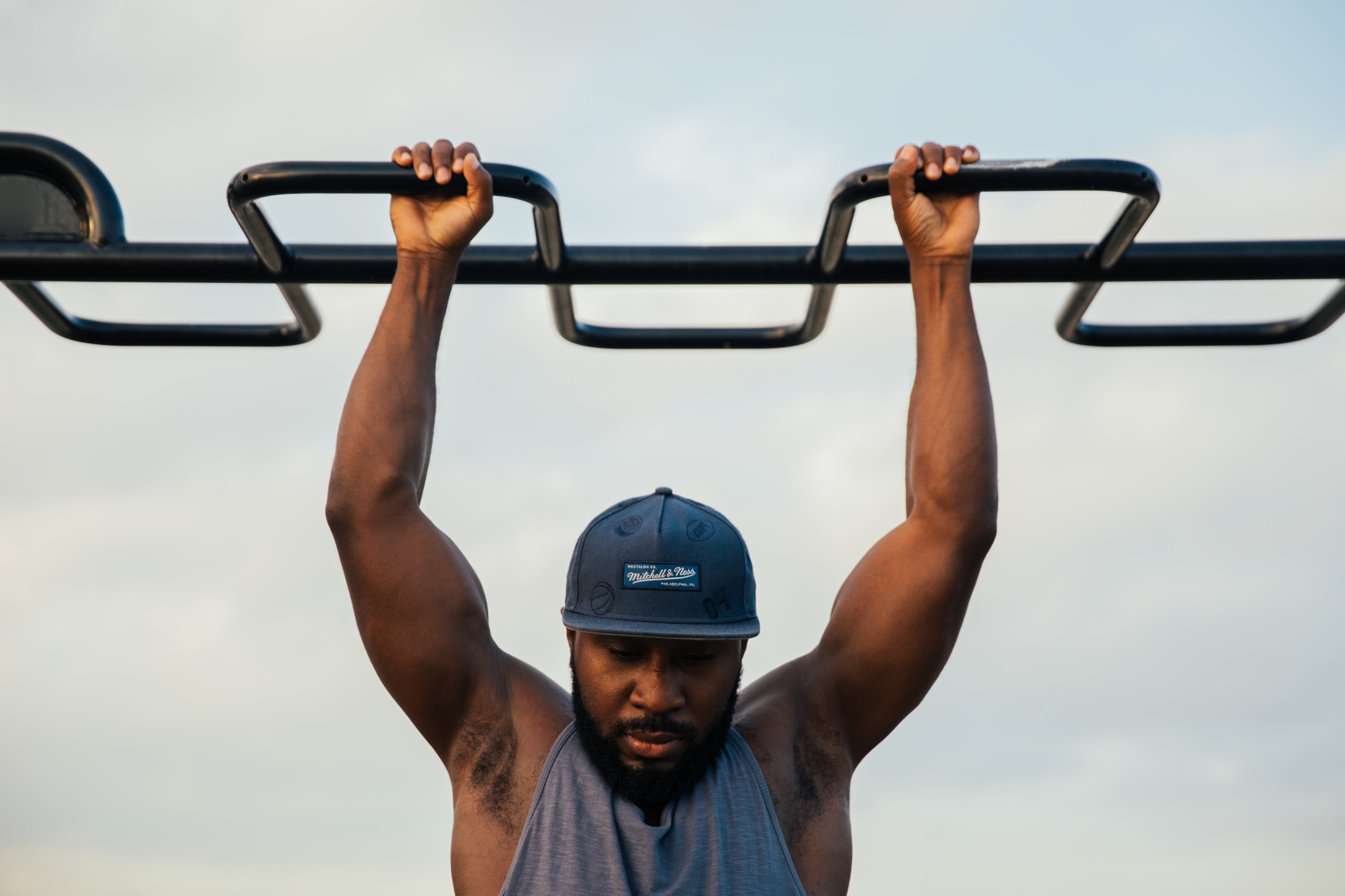 Muscular black man wearing a tank top and hat, hanging on pull up bar